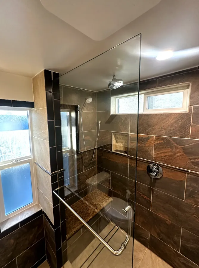 Custom glass shower enclosure with frameless panel and tiled bench in the Tri-Cities